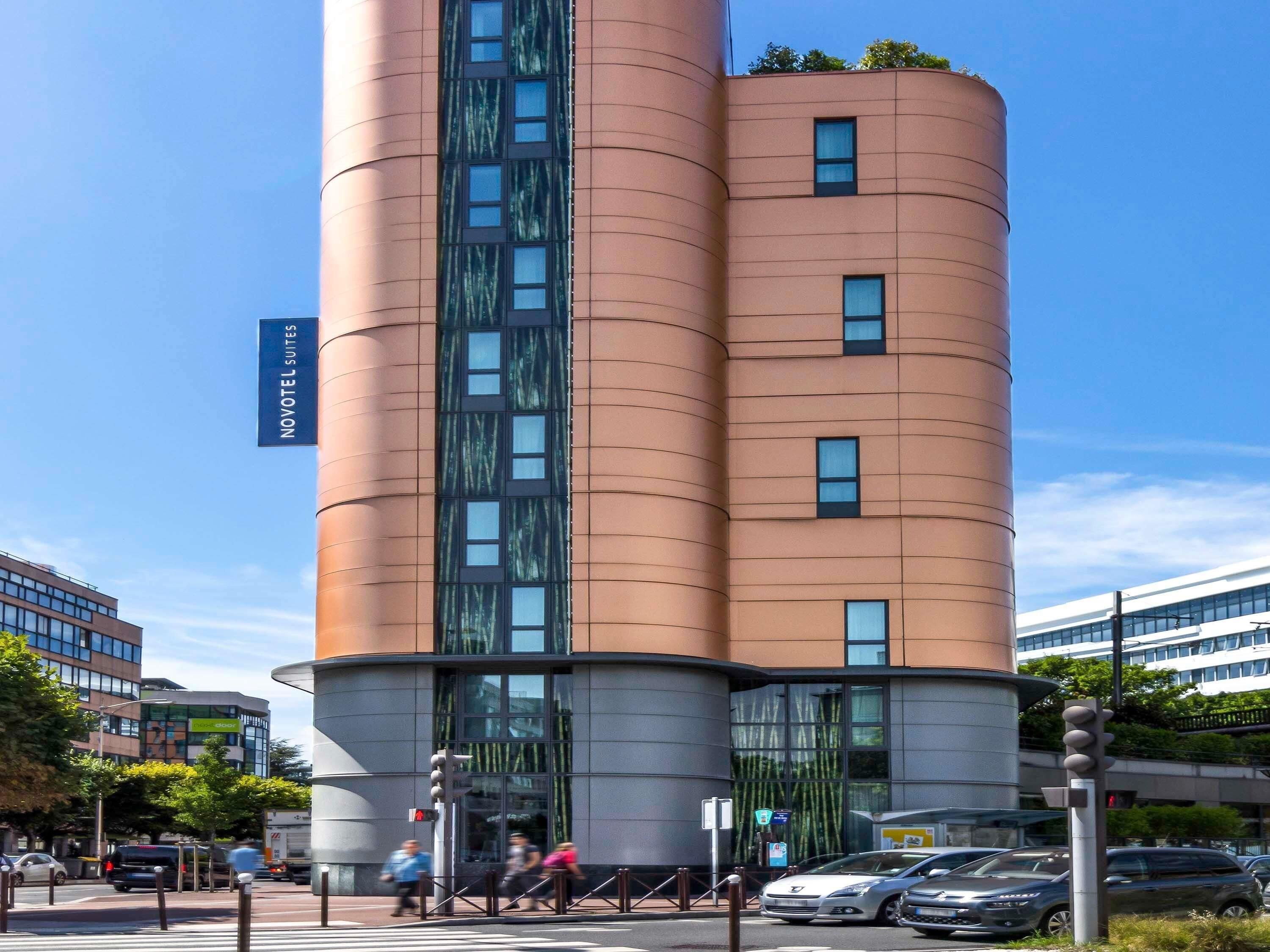 A modern hotel with a cylindrical design, multiple floors, and a sign indicating 'NOVOTEL SUITES'.