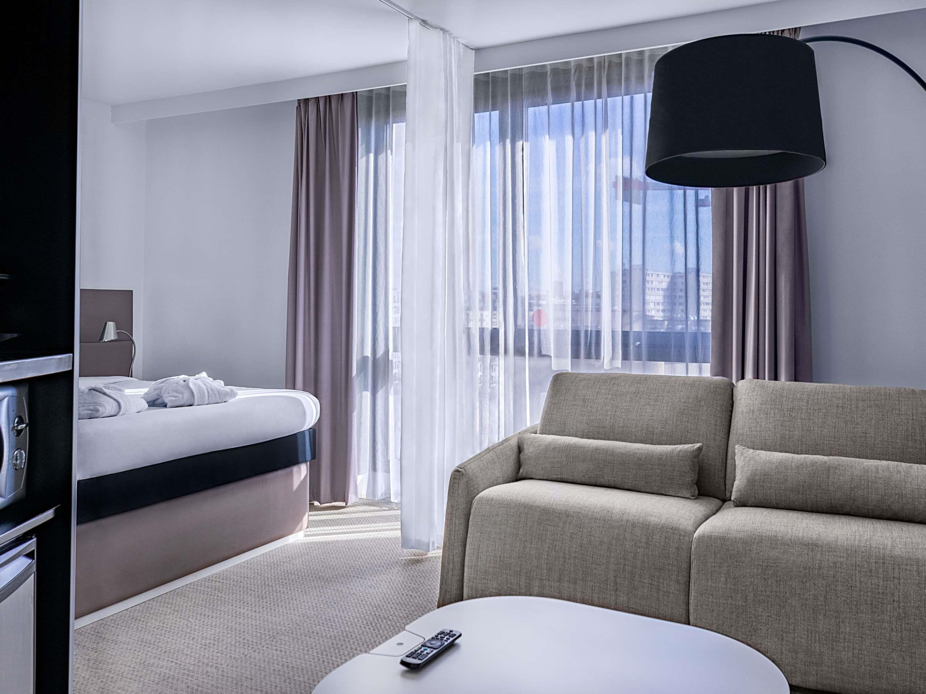 A hotel room with a bed, a sofa, a desk, and a lamp.