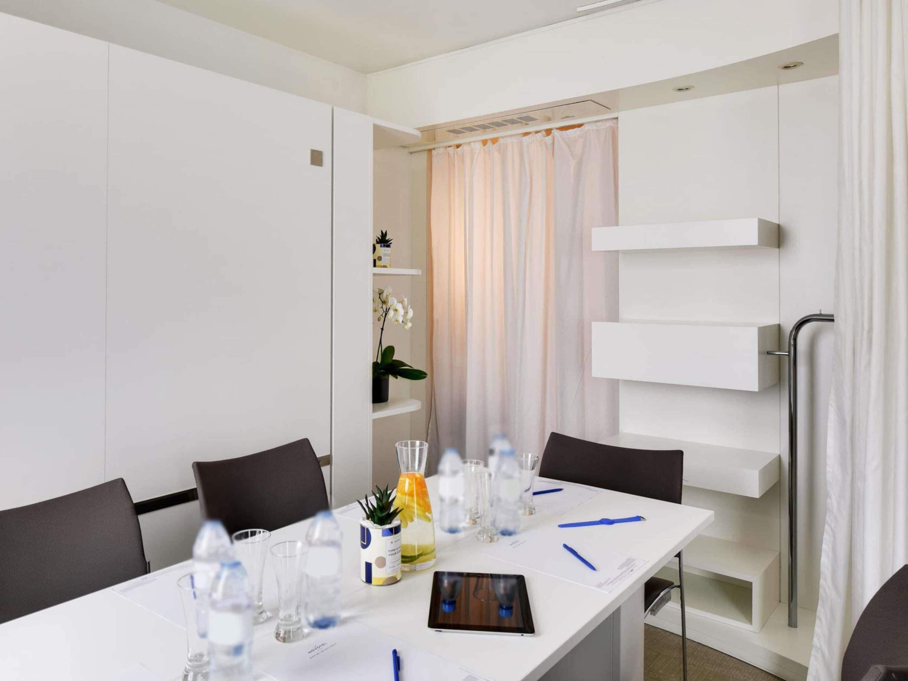 A modern hotel room with a white table, chairs, a whiteboard, and a shower area.