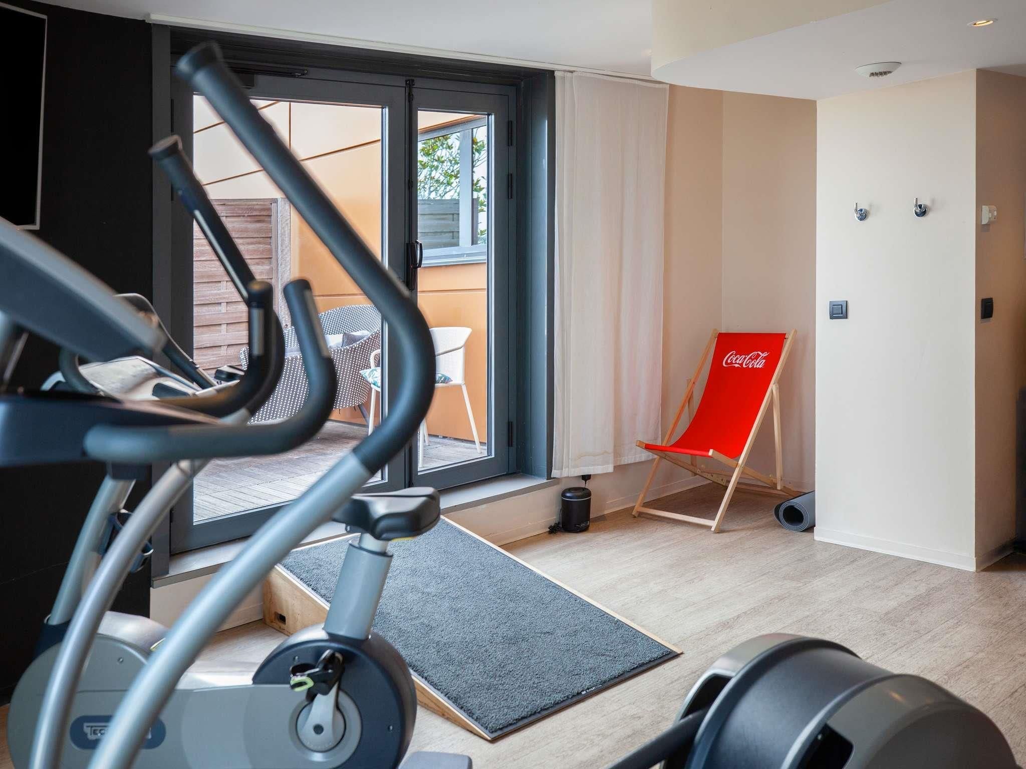 A home gym with exercise equipment, a sliding glass door leading to a patio, and a red Coca-Cola branded chair.