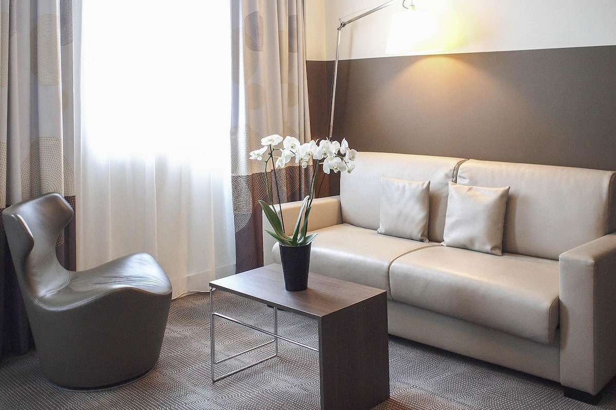A modern hotel room with a sofa, a chair, a coffee table, and a potted orchid.