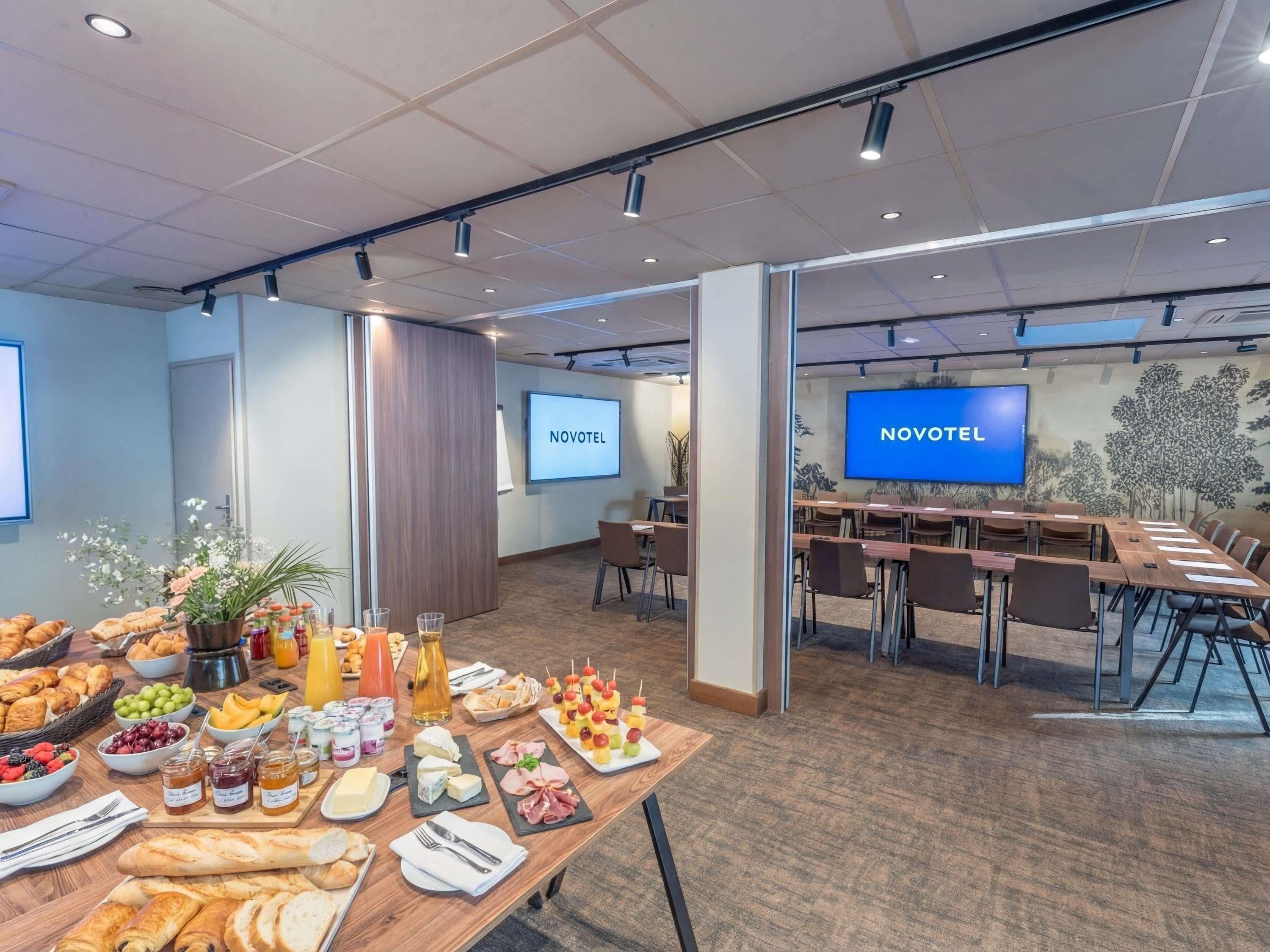 A conference room with a long table set for a buffet, two screens displaying 'NOVOTEL', and a carpeted floor.