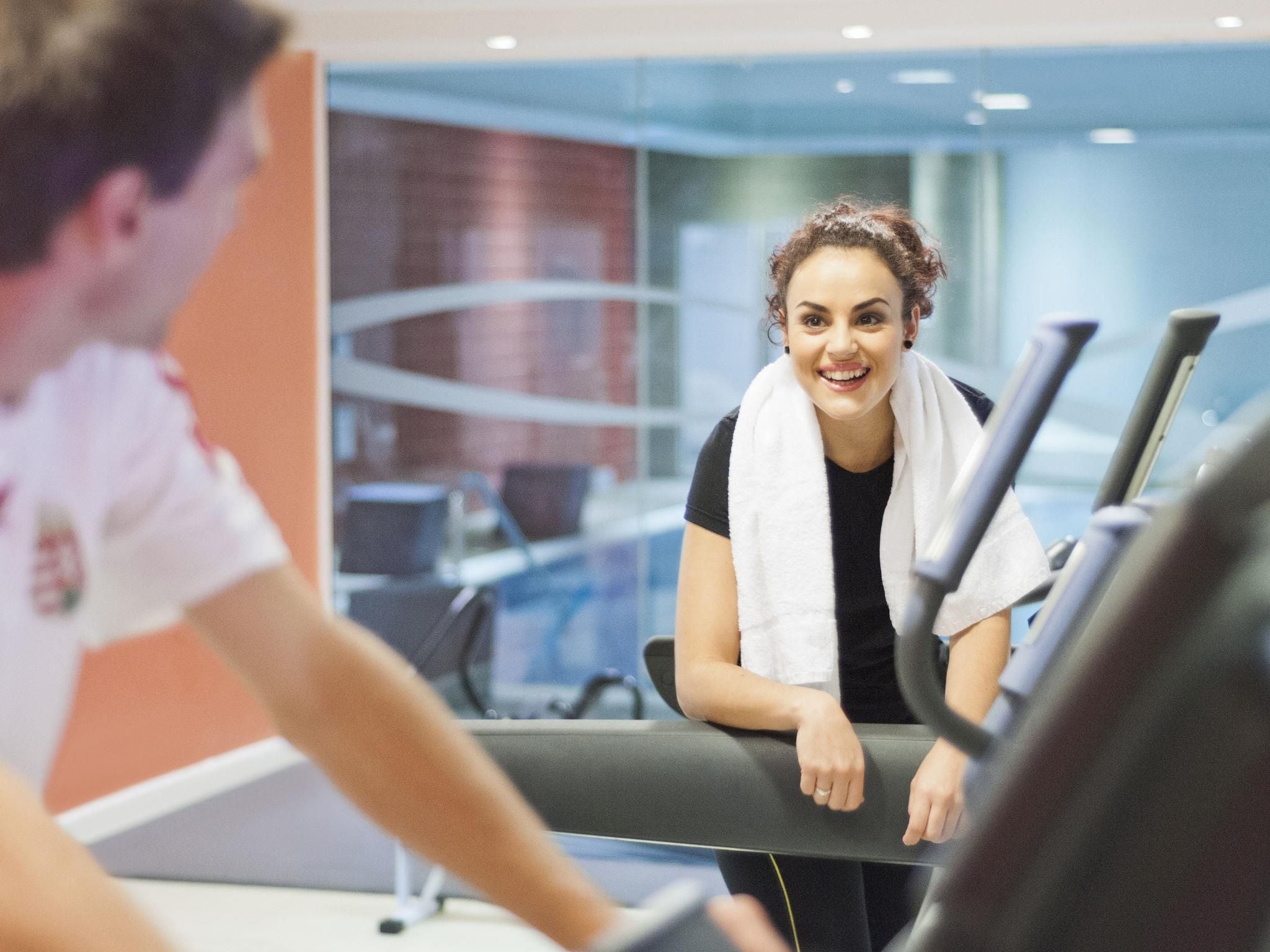 A person using a treadmill in a gym with a glass wall and a red wall in the background.