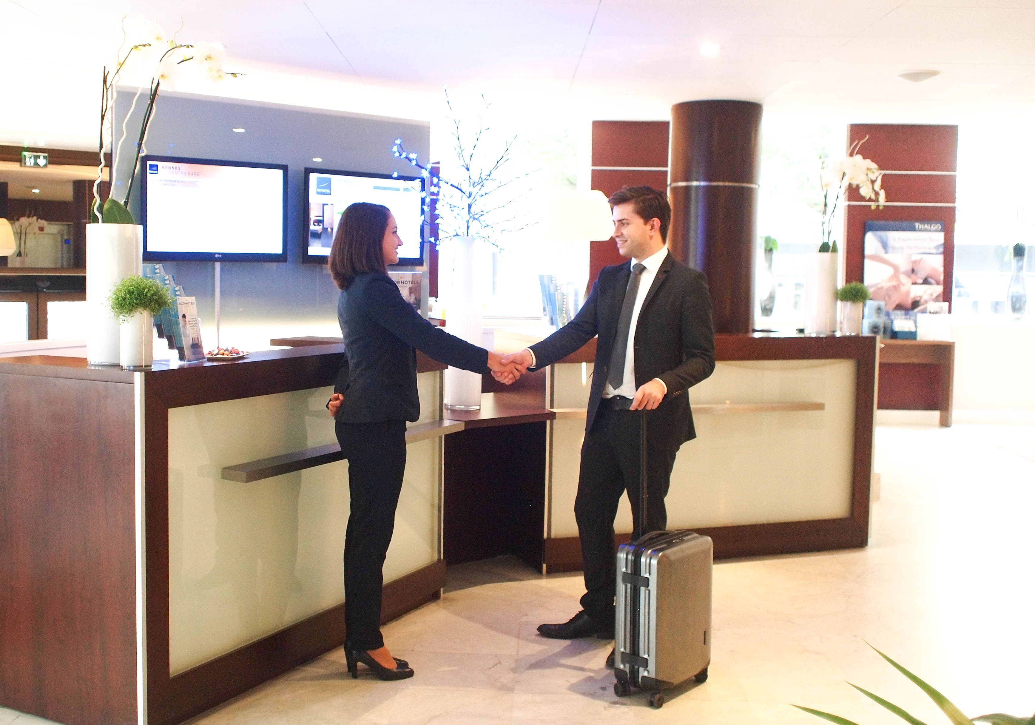 A reception area with a wooden reception desk, two monitors, and a potted plant.