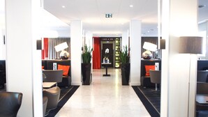 A hotel lobby with a modern design, featuring a reception desk, seating area, and a red curtain.