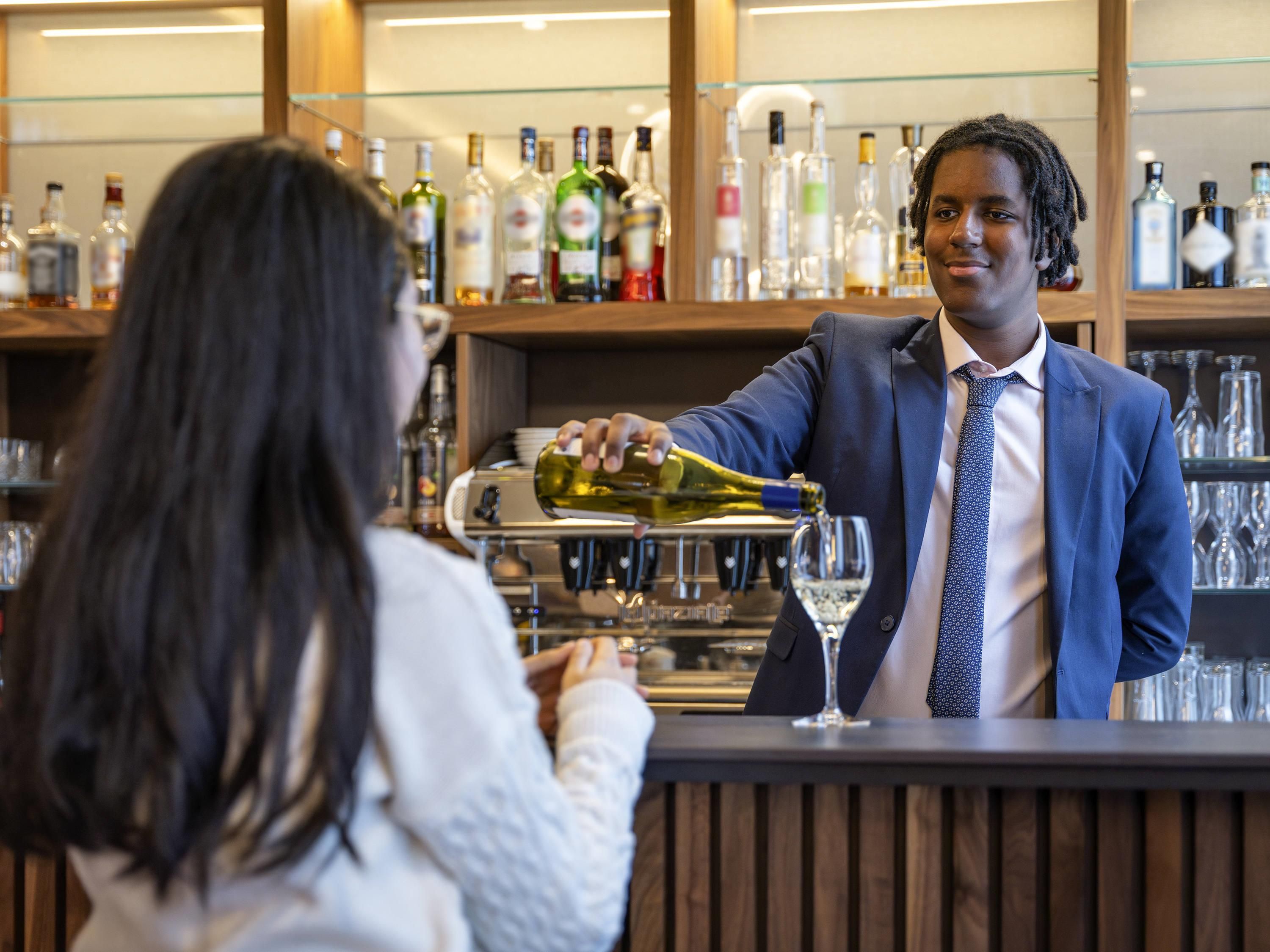 A bar setting with a bartender pouring a drink into a glass.