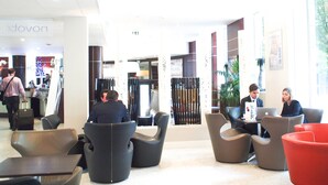 A hotel lobby with modern furniture, a reception desk, and a visible 'Novon' sign.