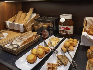 A buffet with various breads, pastries, and condiments including Nutella.