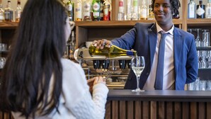A bar setting with a bartender pouring a drink into a glass.