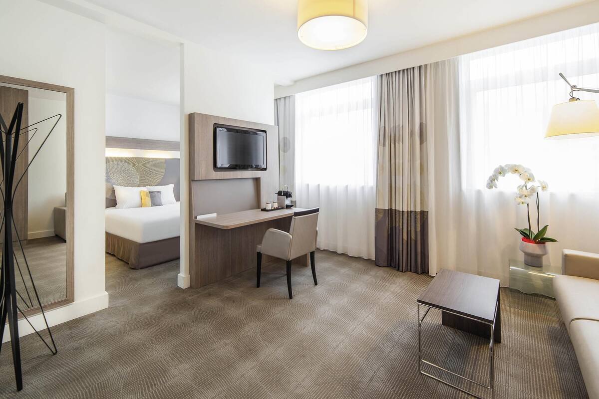 A hotel room with a bed, desk, chair, TV, and a potted plant.