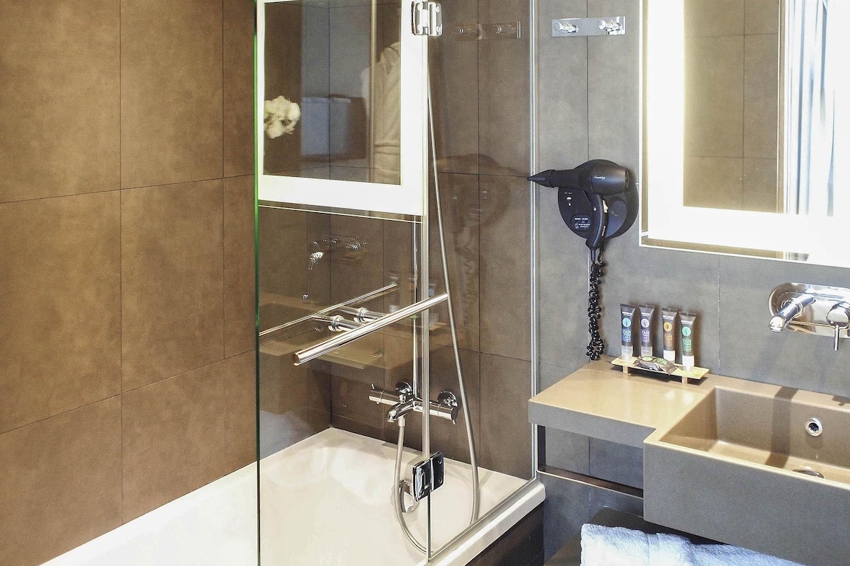A modern bathroom with a glass-enclosed shower, a vanity with a mirror, and a hairdryer on the wall.