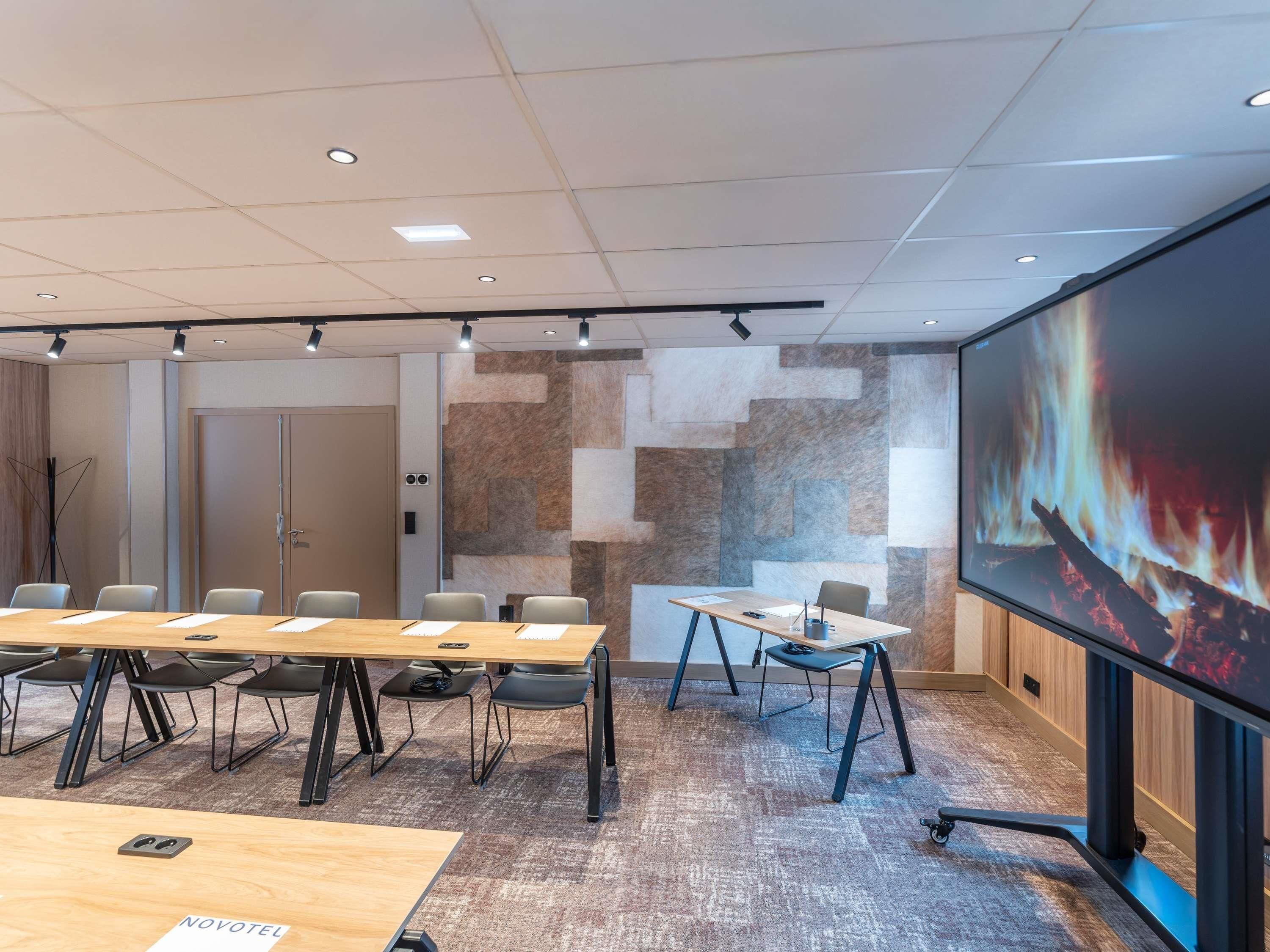 Un salón de conferencias con una pantalla grande, varias mesas y sillas.