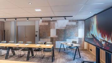 Un salón de conferencias con una pantalla grande, varias mesas y sillas.