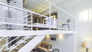 A modern interior with a staircase leading to a loft bedroom, a dining area with a table and chairs, and a small seating area with a sofa.