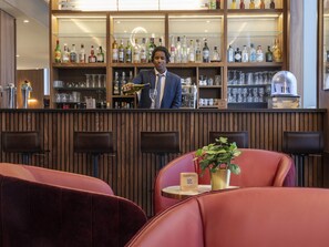 A bar area with a bartender, shelves of liquor bottles, and seating with a plant on a table. - Novotel Spa Rennes Centre Gare (Rennes)