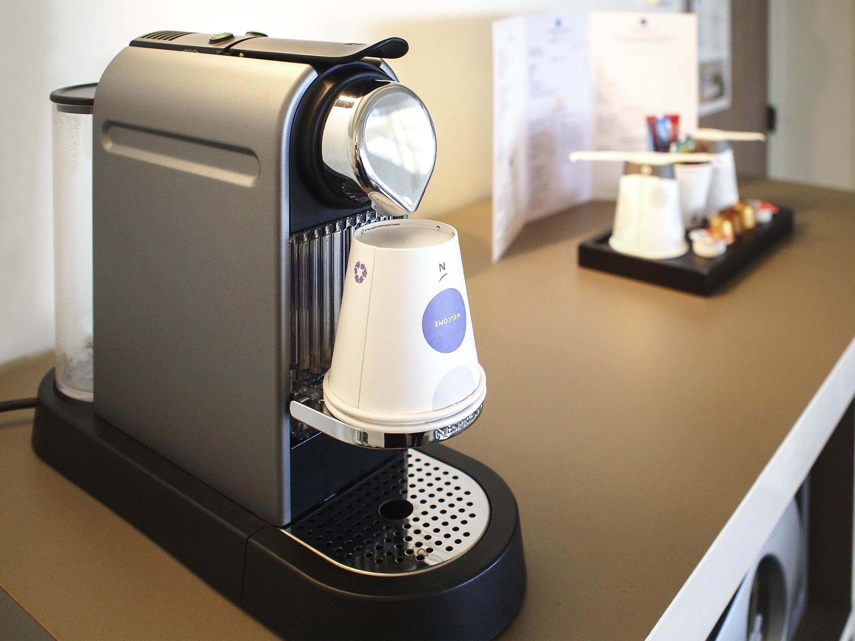 A coffee machine with a cup holder and a tray of pastries on a counter.