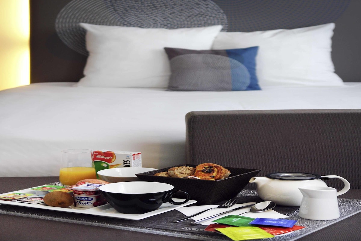 A neatly arranged breakfast tray with a bowl of cereal, a cup, a jug of juice, and a basket of pastries on a tray.