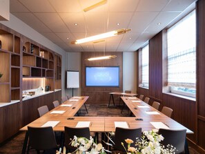 A conference room with a long table, chairs, a projector screen, and wooden shelving. - Novotel Spa Rennes Centre Gare (Rennes)