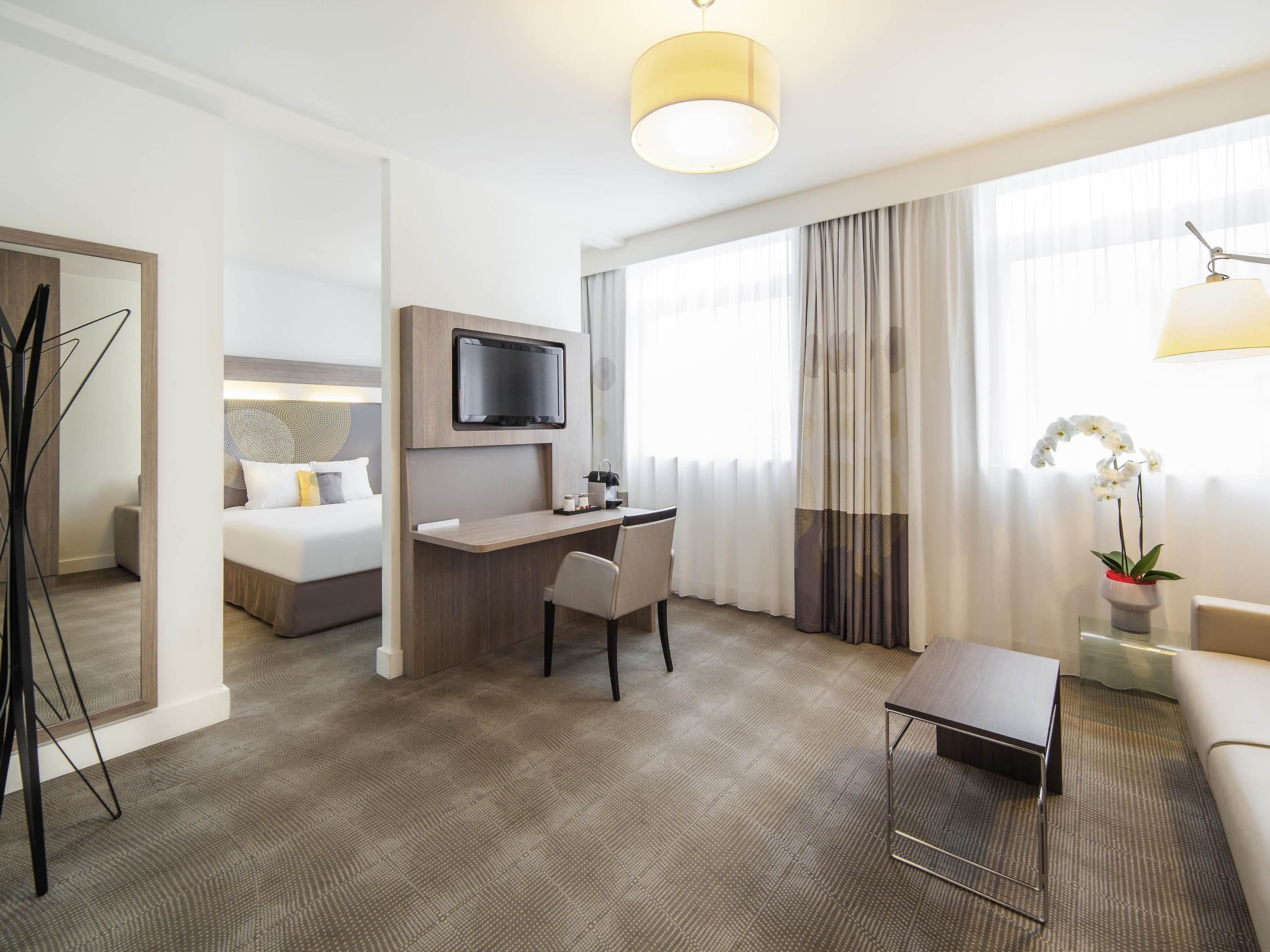 A hotel room with a bed, desk, chair, TV, and a potted plant.