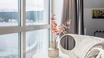 Una habitación con un ventanal grande, una mesa redonda, una silla y un florero con flores.