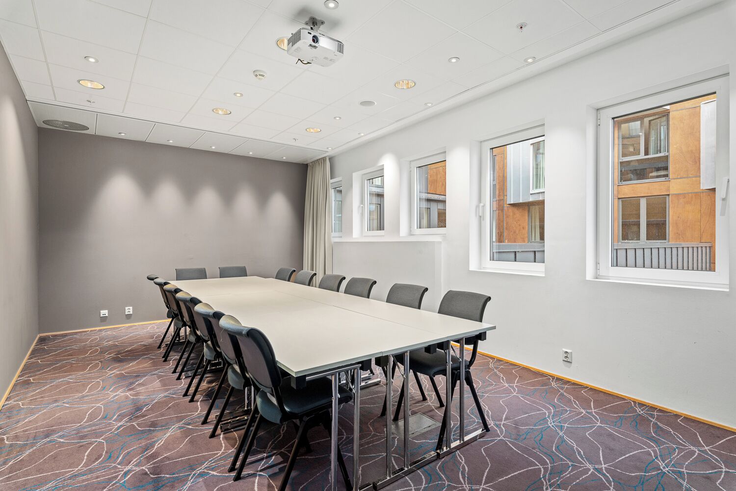A conference room with a long table, chairs, a projector, and large windows with wooden frames.