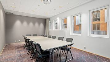 A conference room with a long table, chairs, a projector, and large windows with wooden frames.