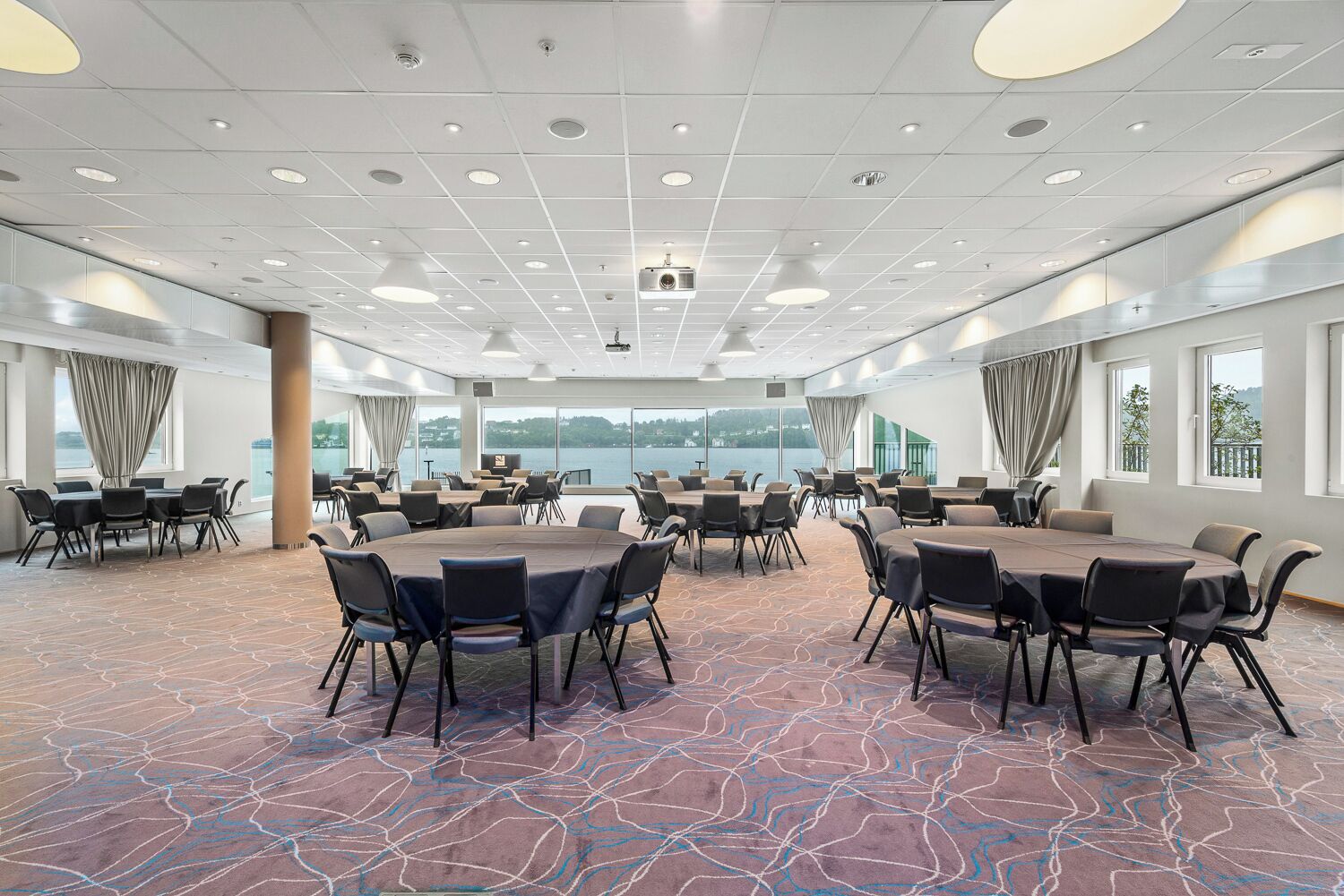 A conference room with round tables and chairs, large windows with curtains, and a patterned carpet.