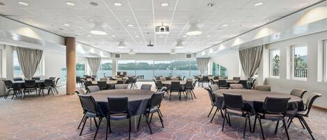 A conference room with round tables and chairs, large windows with curtains, and a patterned carpet.