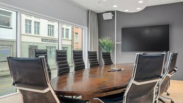 A conference room with a round table, black leather chairs, and a large screen.