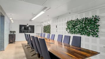 Een vergaderruimte met een lange houten tafel, blauwe stoelen, een grote wand van groene planten en een wandgemonteerde televisie.