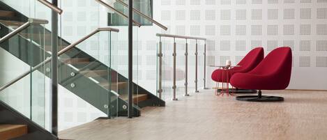 A modern interior with a staircase, glass railings, and red chairs.