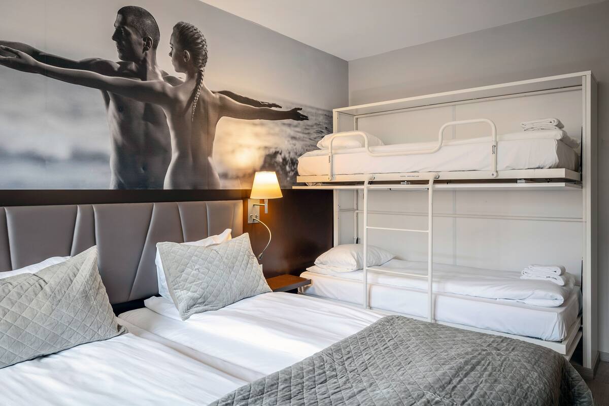 A hotel room with a bed, a nightstand, a lamp, a wall-mounted TV, and a bunk bed.