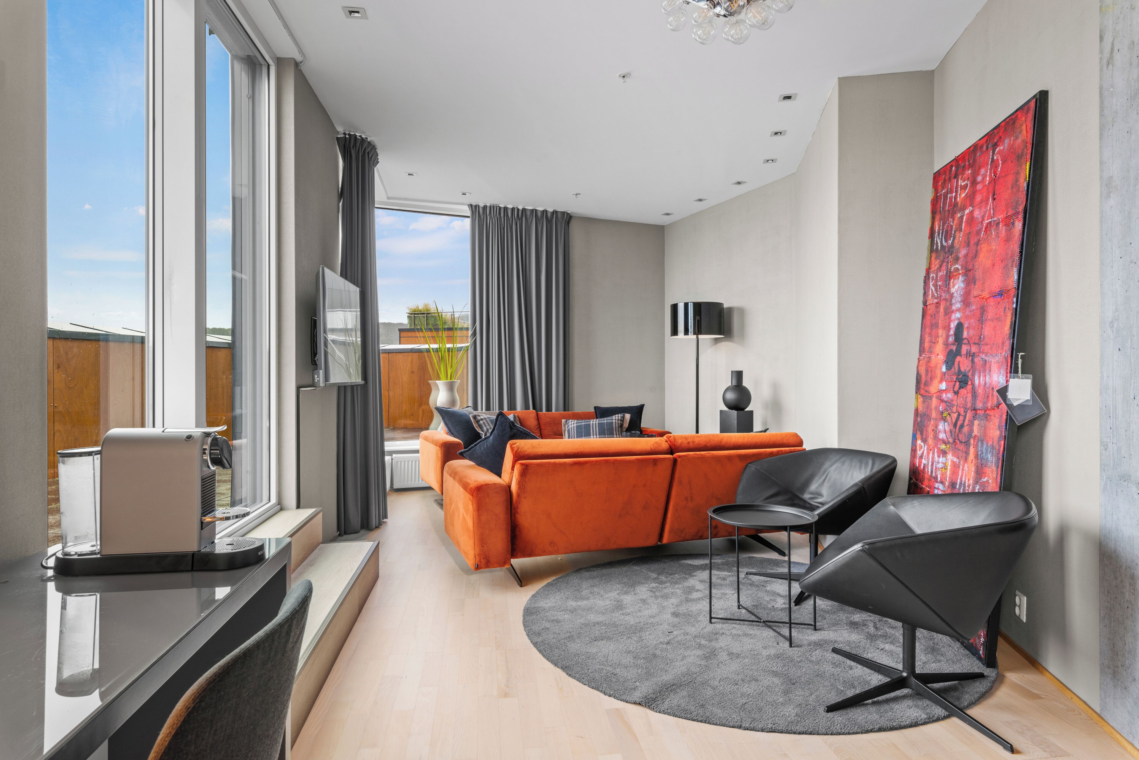 A modern living room with a sofa, a chair, a coffee machine, and a large window.