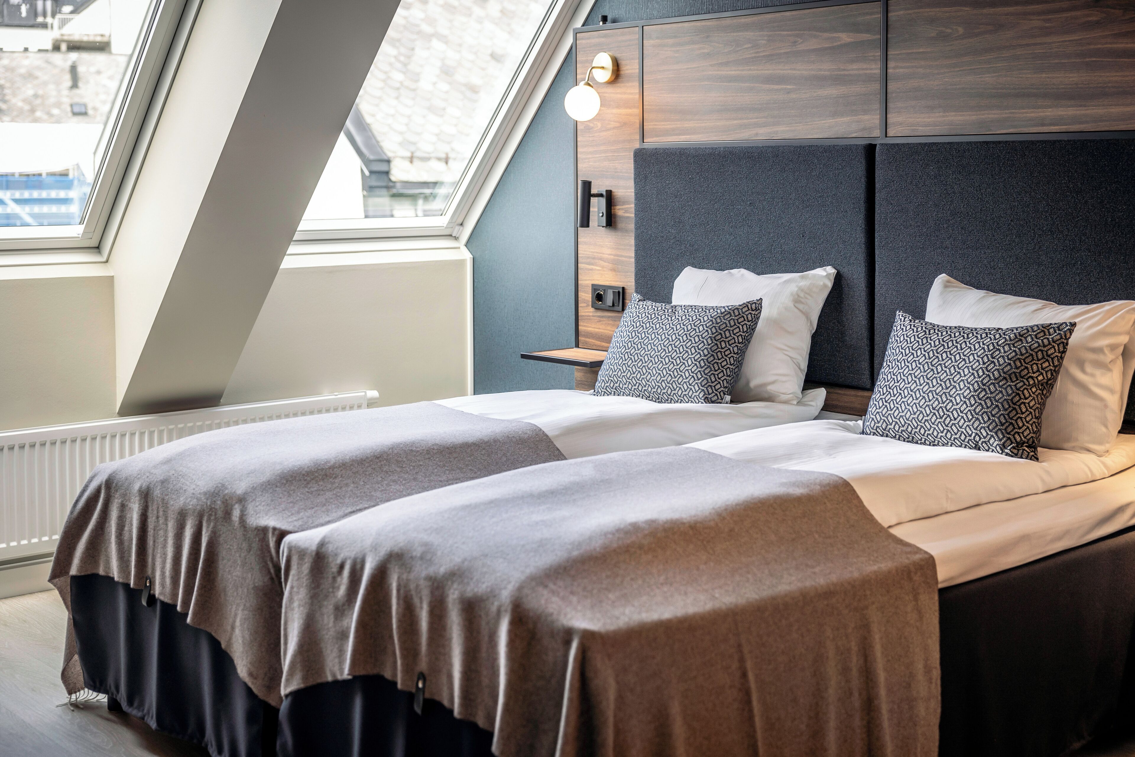 Une chambre à coucher moderne avec une lucarne, un lit agrémenté d’oreillers à motifs et une table de chevet avec une lampe.