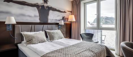 A hotel room with a large bed, two bedside lamps, a chair, and a large window with curtains.