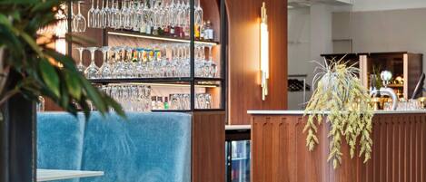 Zona de bar moderna con mostrador de madera, asientos acolchados azules y una vitrina para copas.