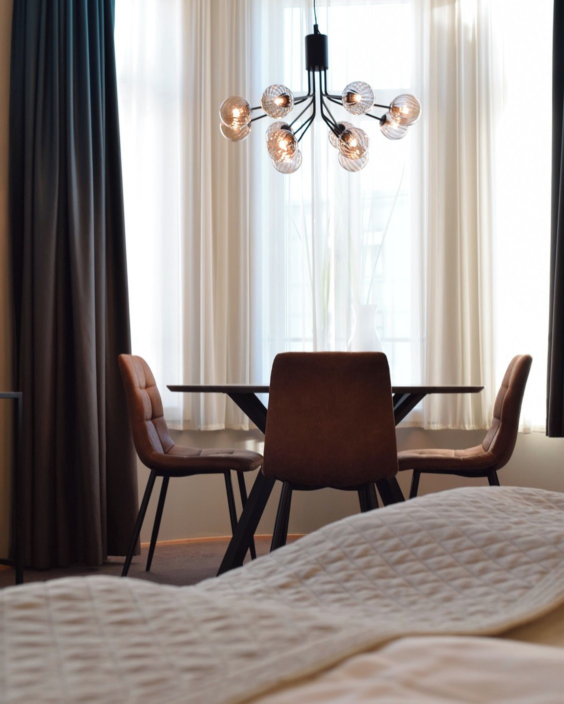 A hotel room with a bed, a dining table with chairs, and a chandelier.
