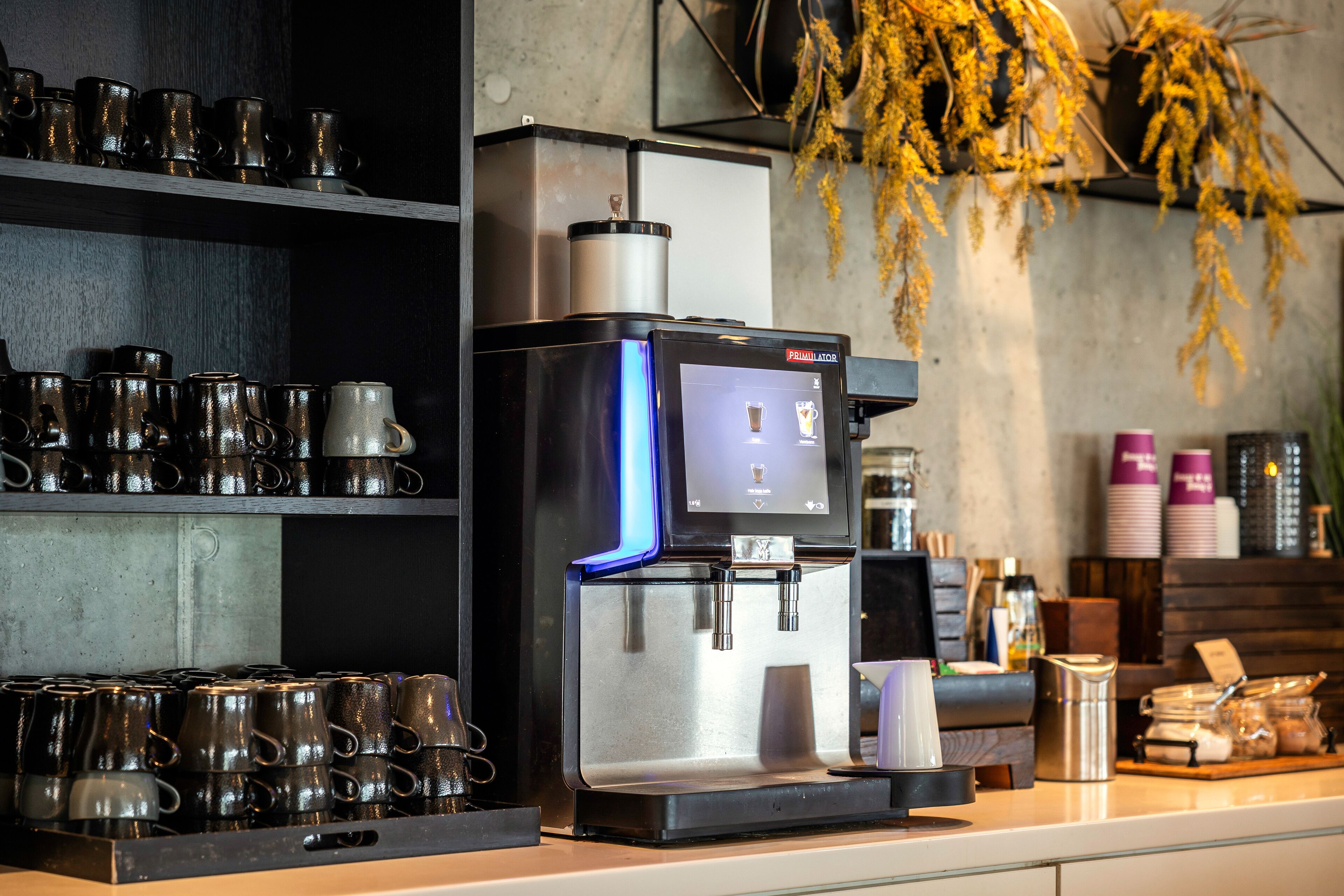 A coffee machine with a digital display, a coffee grinder, and a variety of mugs on shelves.