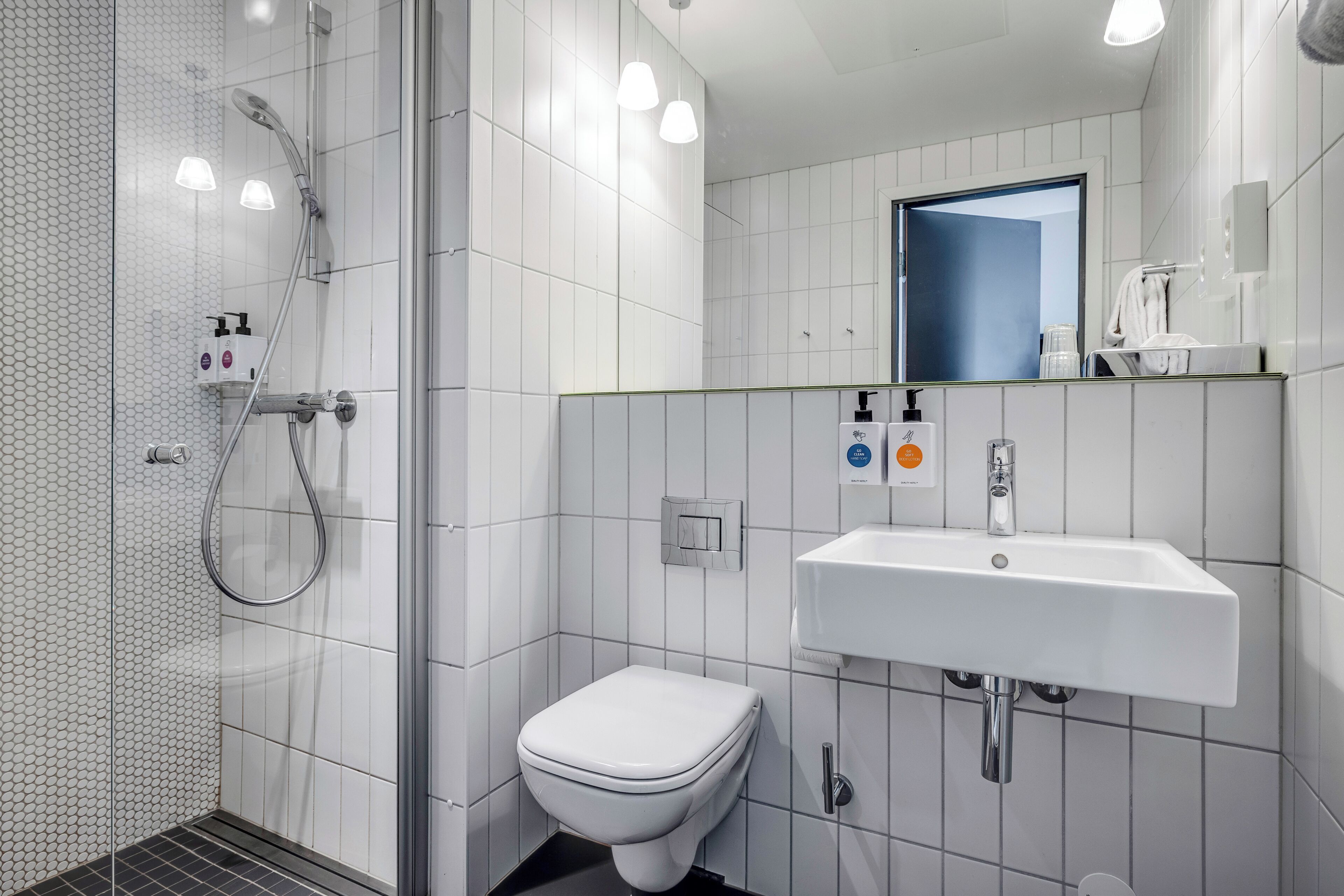 A modern bathroom with a shower, toilet, and sink, featuring a tiled wall and a mirror above the sink.