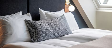 A neatly made bed with a patterned pillow, a headboard, and a window with a view of the outside.