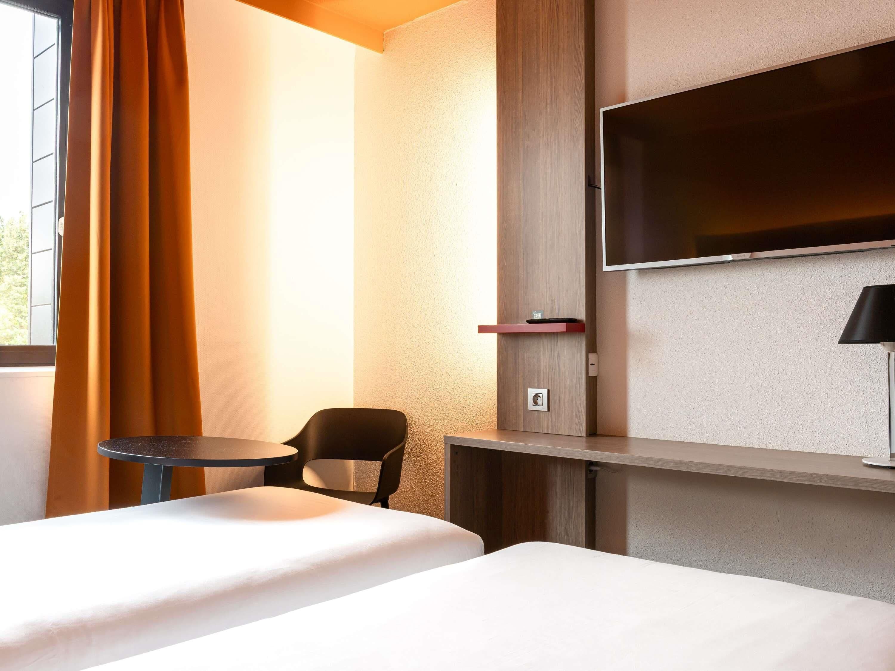 Habitación de hotel con una cama, una silla, un televisor montado en la pared y una mesita.