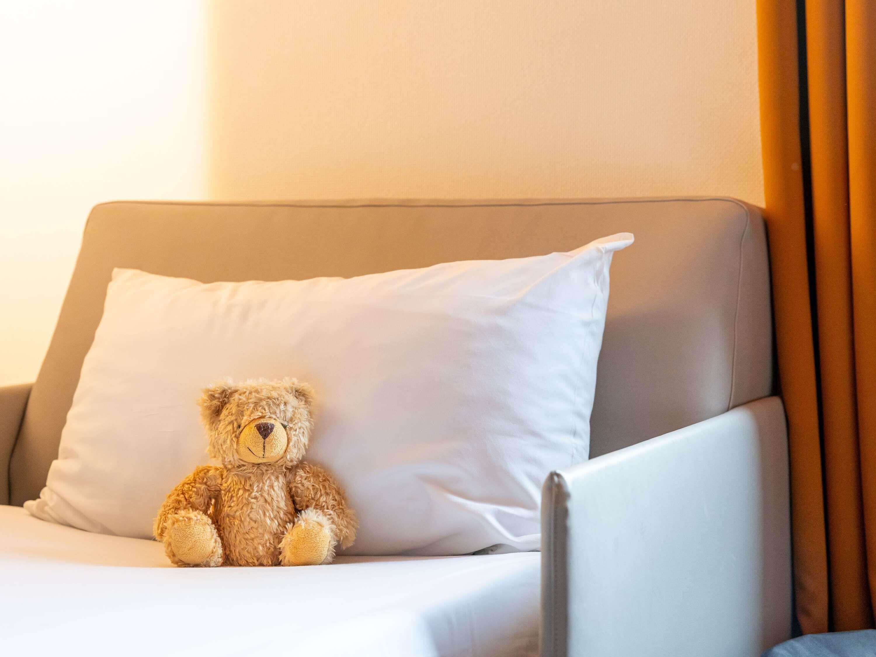 Un sofá beige con un cojín blanco y un oso de peluche.