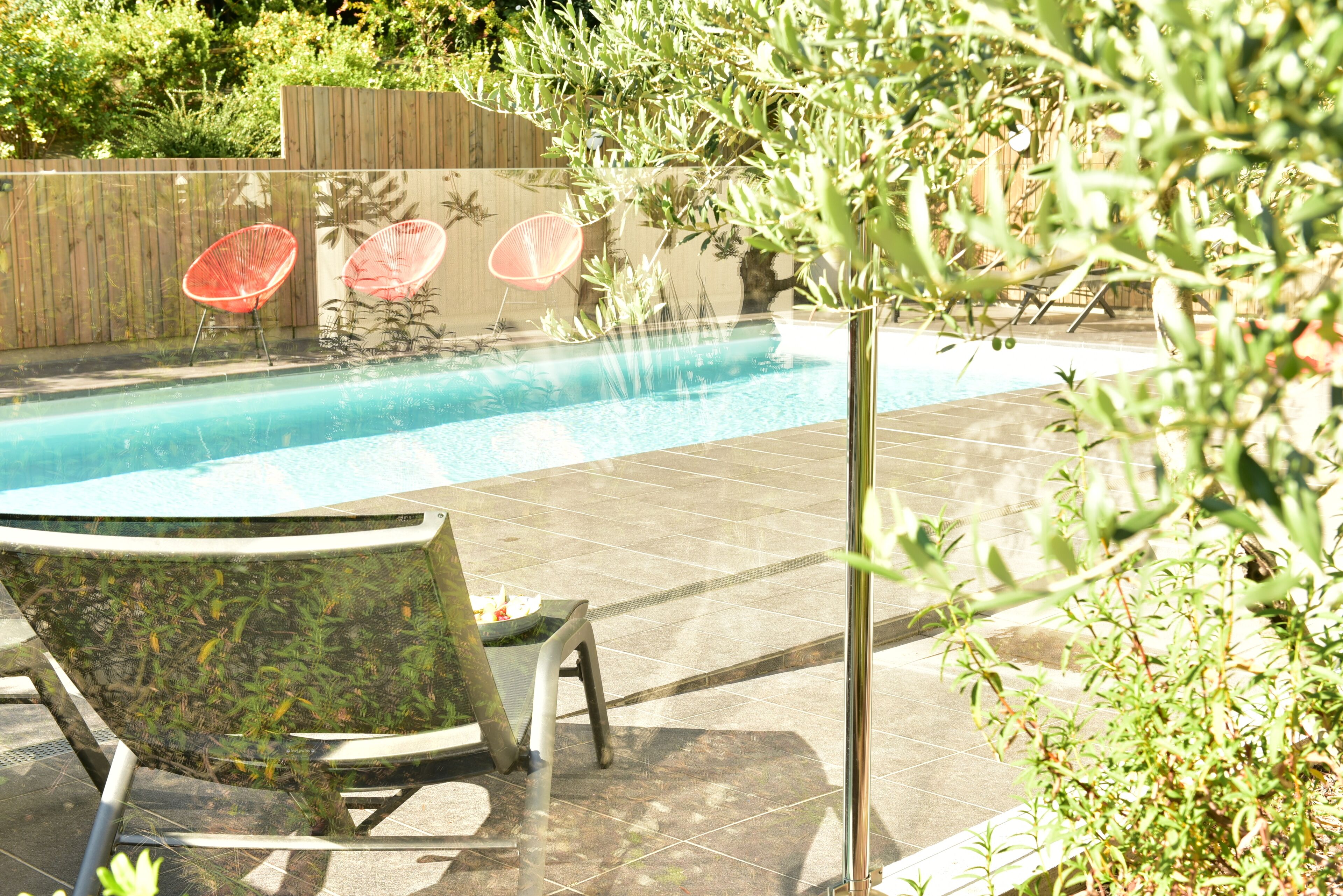 Una piscina con suelo de baldosas, rodeada de vegetación y una valla de madera.