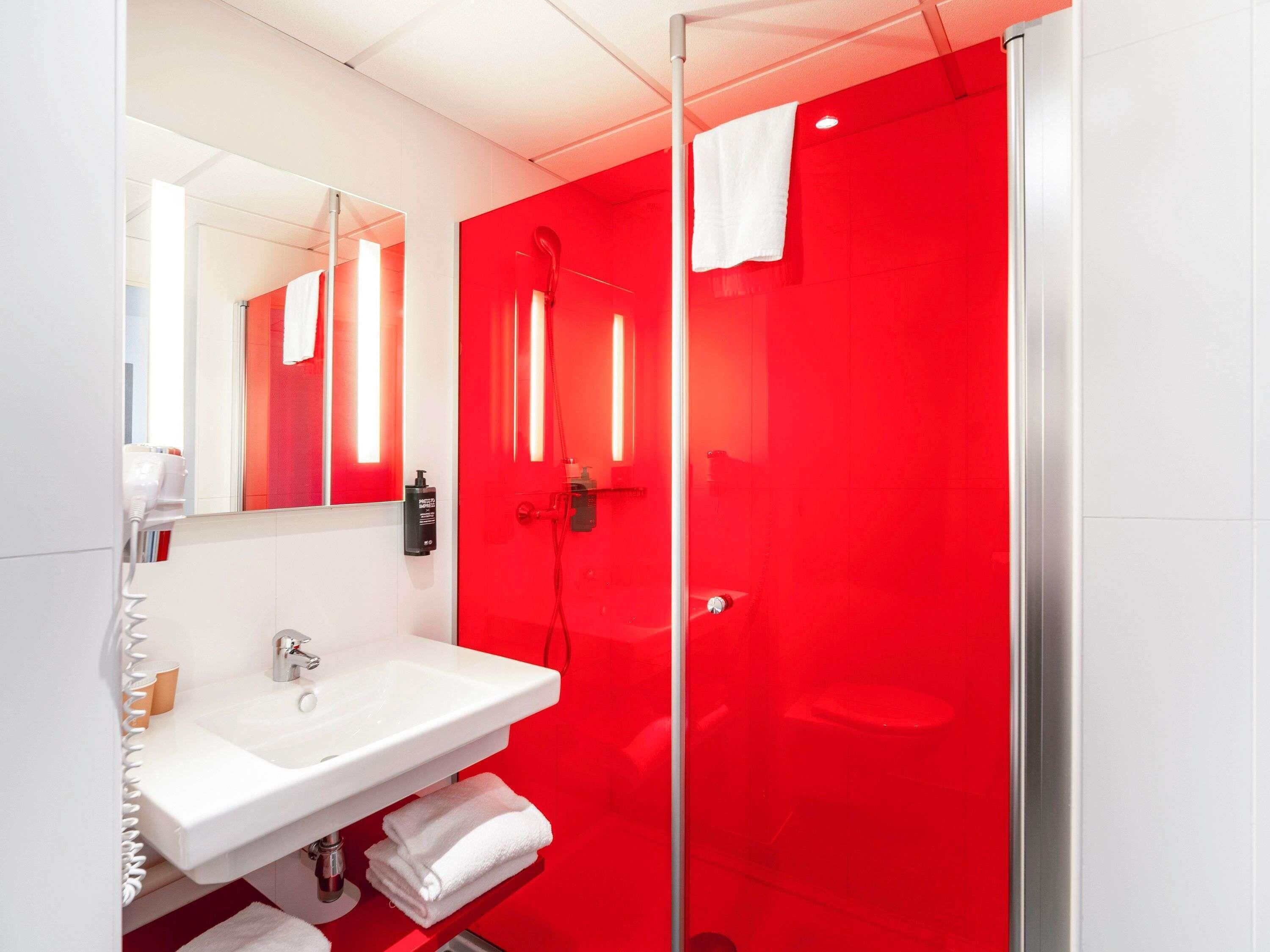 Ein modernes Badezimmer mit einem weißen Waschbecken, einer Duschkabine aus Glas und einer roten Akzentwand.