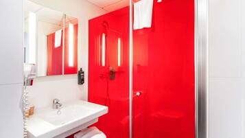 Ein modernes Badezimmer mit einem weißen Waschbecken, einer Duschkabine aus Glas und einer roten Akzentwand.