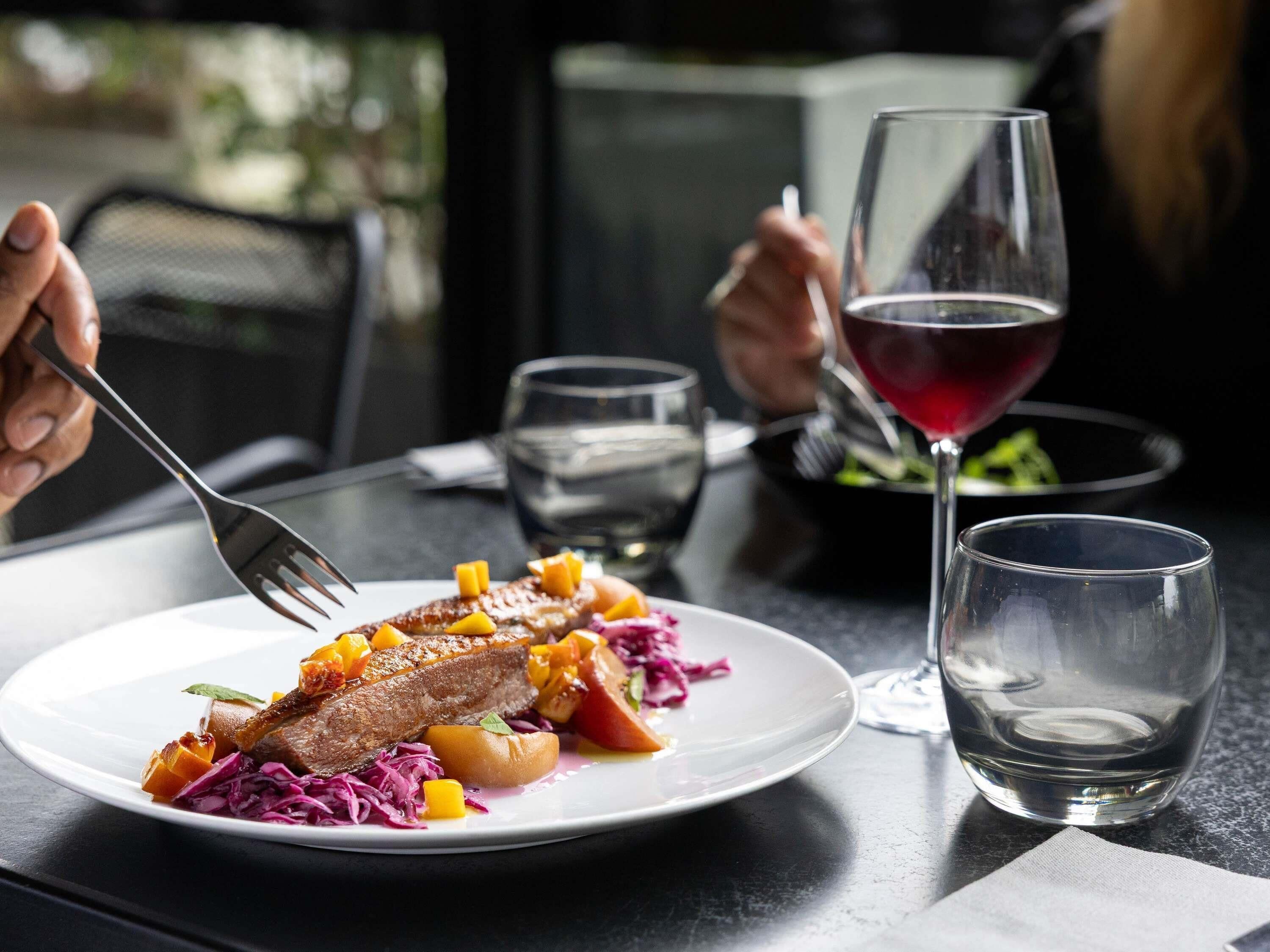 Una mesa de comedor con un plato de comida, una copa de vino tinto y un vaso de agua.