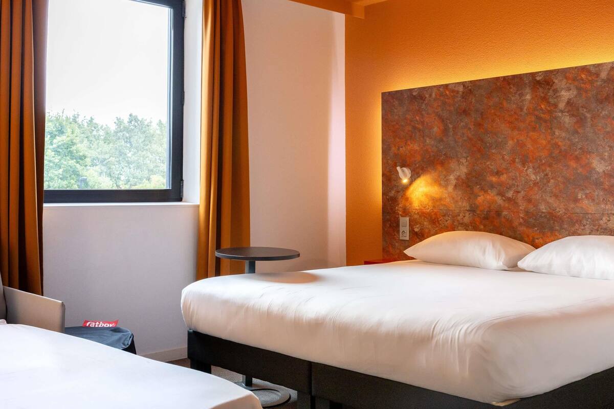 Une chambre d’hôtel avec un lit, une petite table ronde et une vue sur les arbres par la fenêtre.