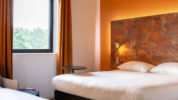 Et hotelværelse med en seng, et lille rundt bord og udsigt til træer gennem vinduet.