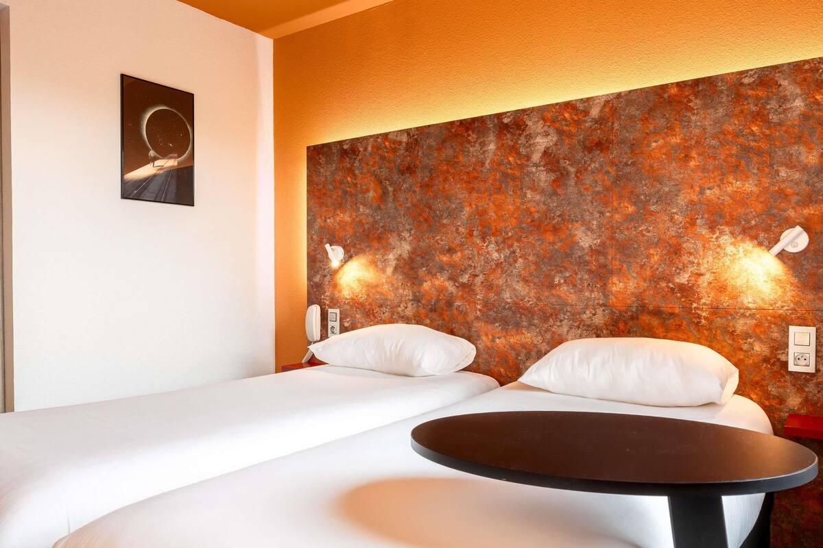 Une chambre d’hôtel avec un lit, une table de chevet et un mur orné d’une fresque à motifs.
