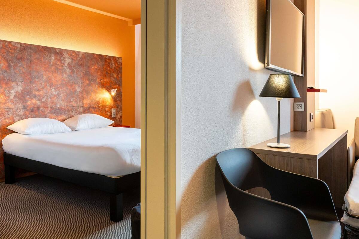 Une chambre d’hôtel avec un lit, un bureau, une chaise, un miroir et un mur à texture.